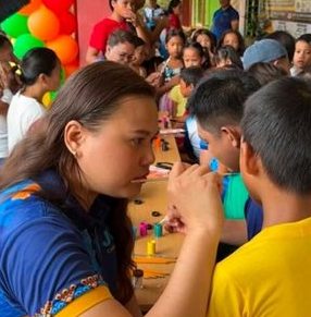 A JCI volunteer face-painting a child at the Bags of Hope area launching